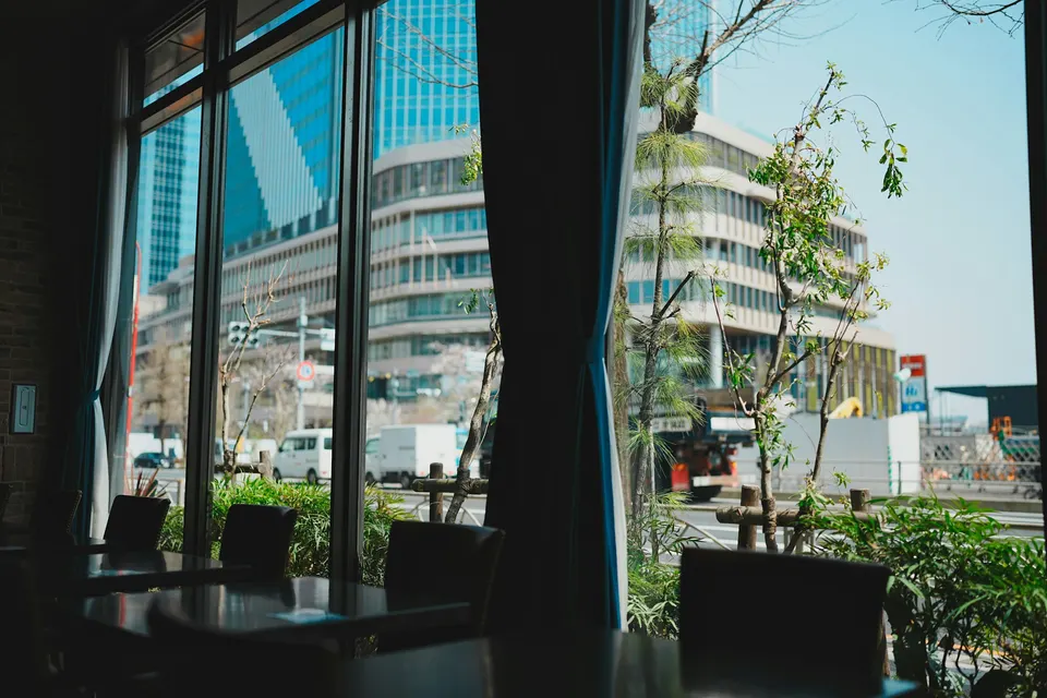 Salão de café com janelas altas e prédios da cidade lá fora